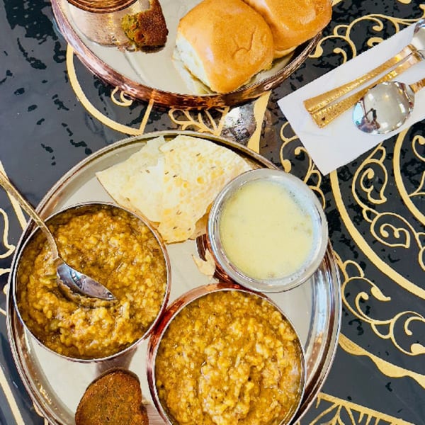 A MaanKi Thali with two bowls of dal, flatbread, a fried patty, and a drink.