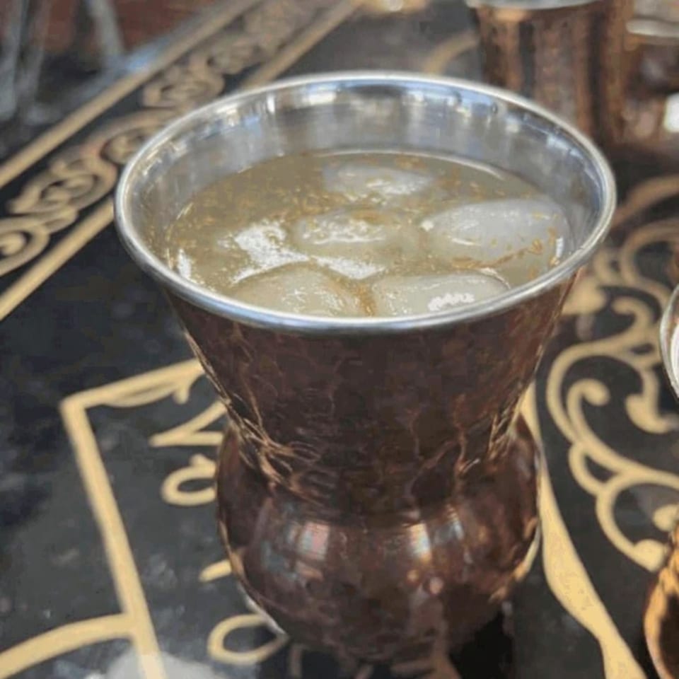 A refreshing Indian drink with ice in a hammered copper cup on a decorative table.