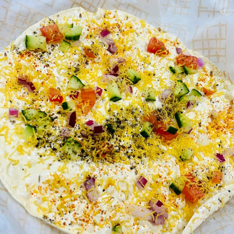 Close-up of Indian street food with white sauce, diced vegetables, and yellow crispy toppings.