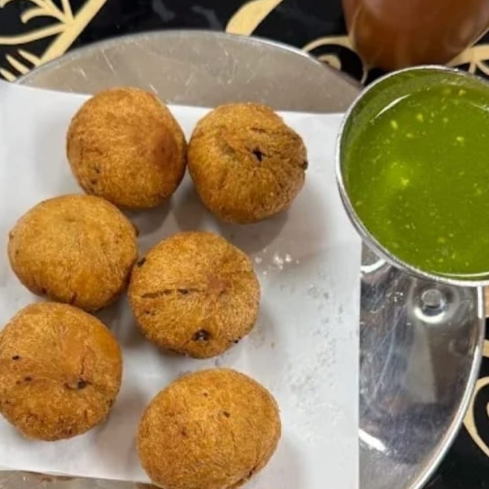 Six golden-brown Indian street food fritters on white paper, with a side of vibrant green chutney.