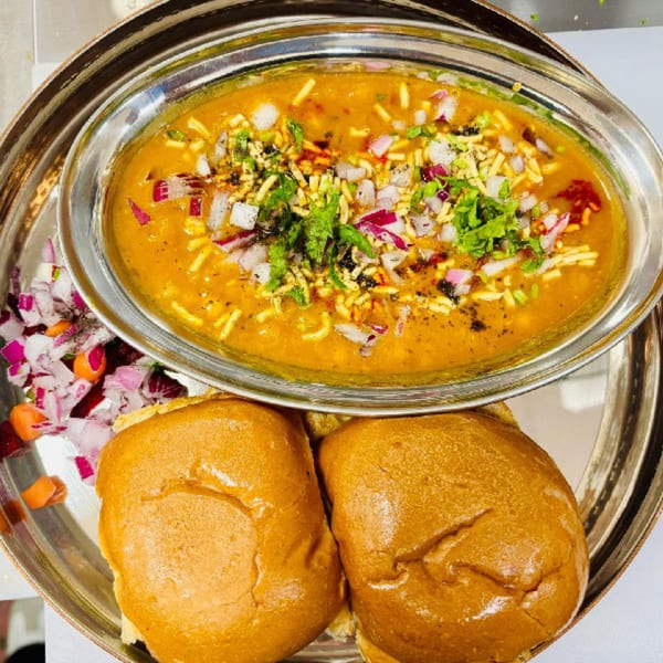 MaanKi Thali's Misal Pav, a spicy Indian curry with pav bread, onions, and cilantro.