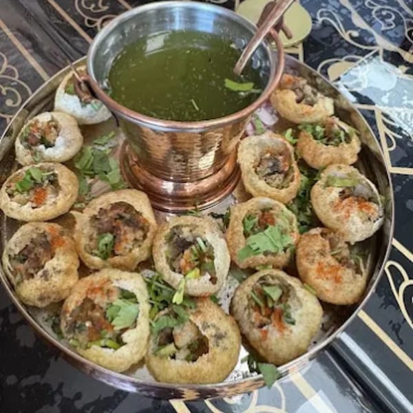 A silver platter of MaanKi Thali's pani puri, filled with spiced potatoes and chickpeas, served with green pani.