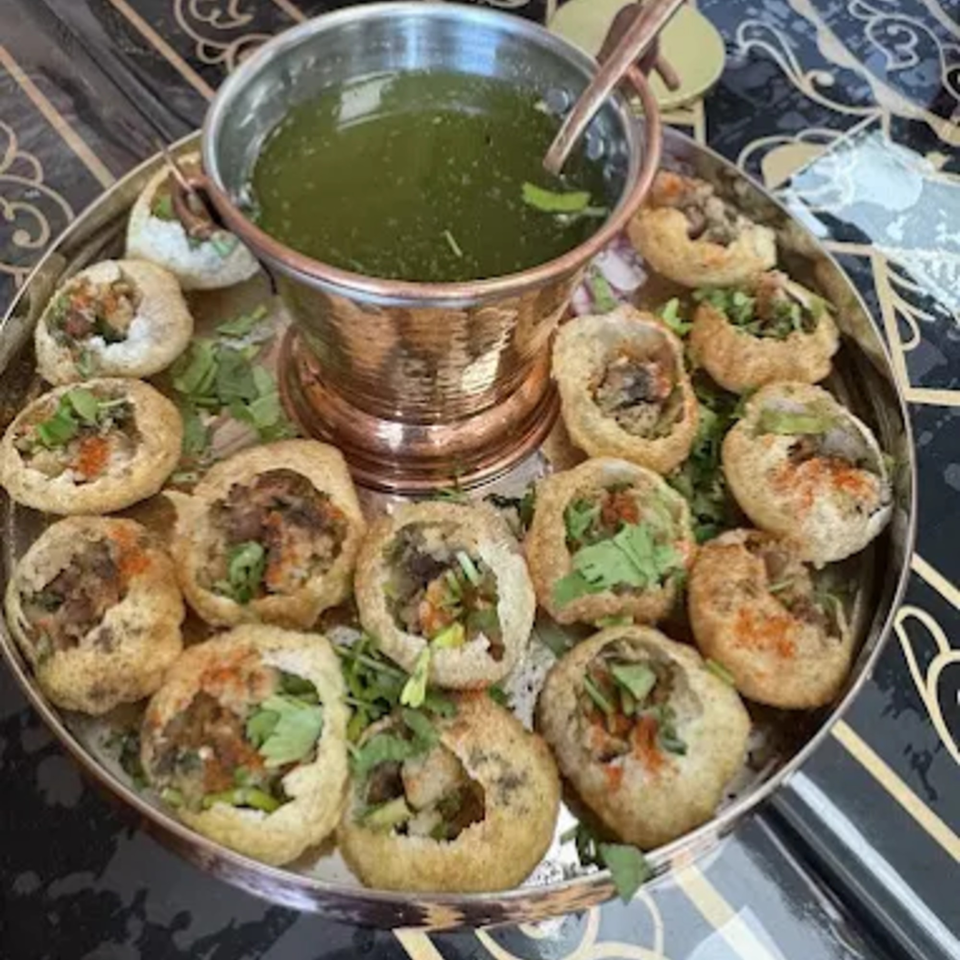 A silver platter of MaanKi Thali's pani puri, filled with spiced potatoes and chickpeas, served with green pani.