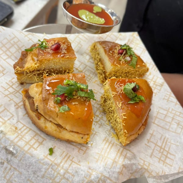 Four pieces of Indian street food, possibly MaanKi Thali, with sauce and garnishes on parchment paper.