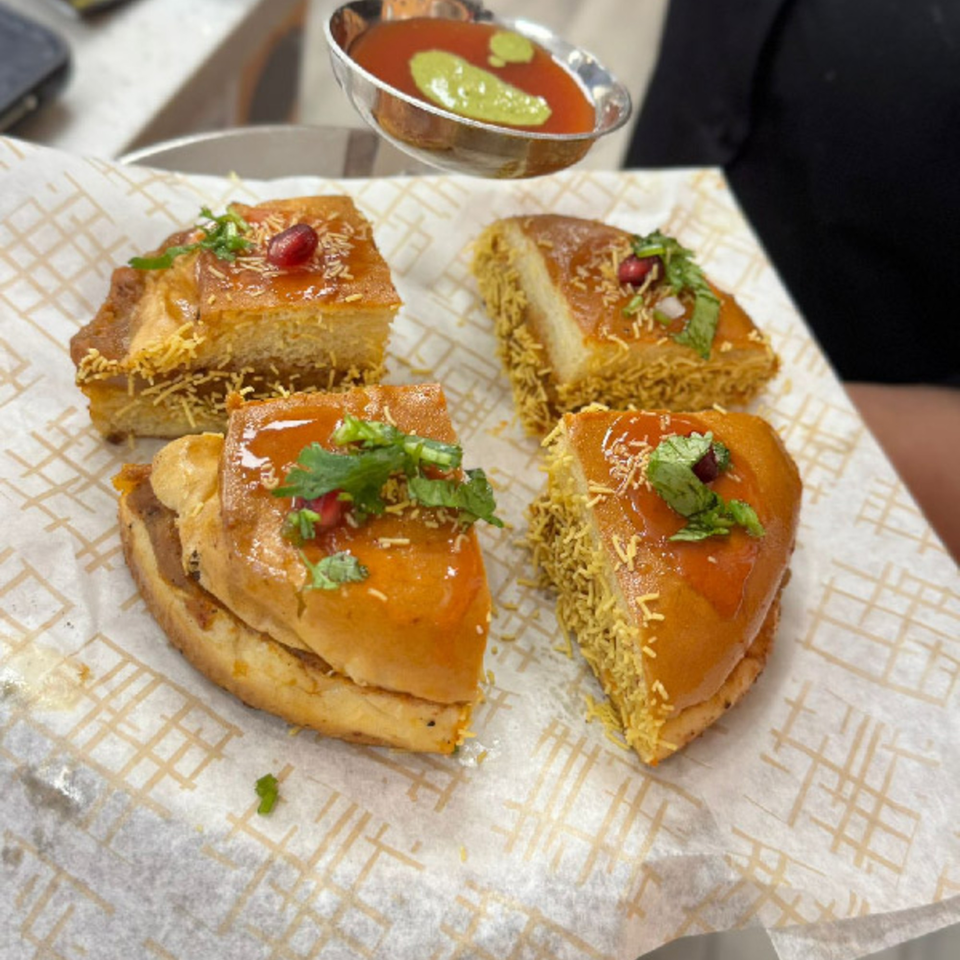 Four pieces of Indian street food, possibly MaanKi Thali, with sauce and garnishes on parchment paper.