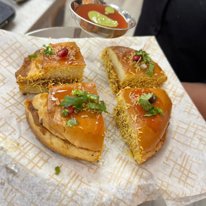 Four pieces of Indian street food, possibly MaanKi Thali, with sauce and garnishes on parchment paper.
