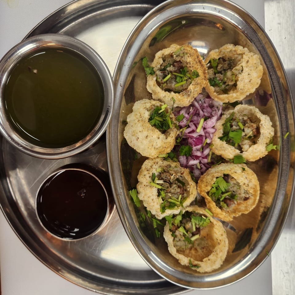 A metal tray with six pani puri, two bowls of sauce, and chopped red onions.