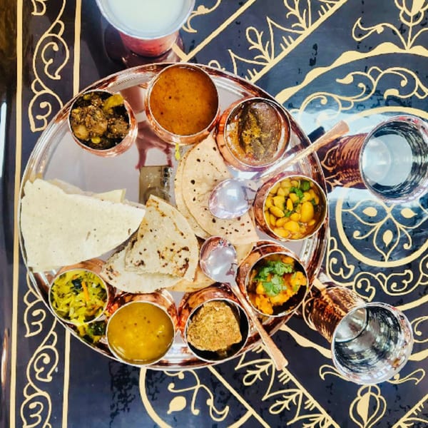 Overhead view of a MaanKi Thali with various Indian dishes, flatbreads, and drinks on a decorative table.