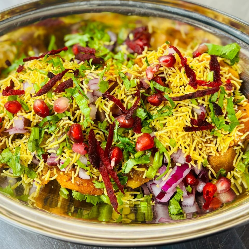 Close-up of Indian street food chaat, topped with sev, pomegranate, red onion, and cilantro.