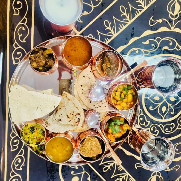 Overhead view of a MaanKi Thali platter with various Indian dishes, flatbreads, and drinks.