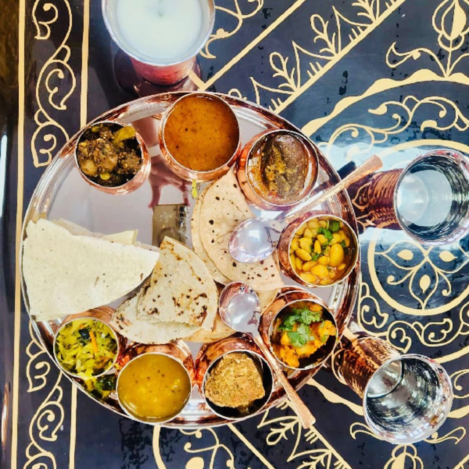 Overhead view of a MaanKi Thali platter with various Indian dishes, flatbreads, and drinks.
